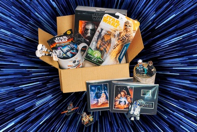 An open Smugglers Crate subscription box filled with Star Wars merchandise like figurines, key chains, mugs and cards.