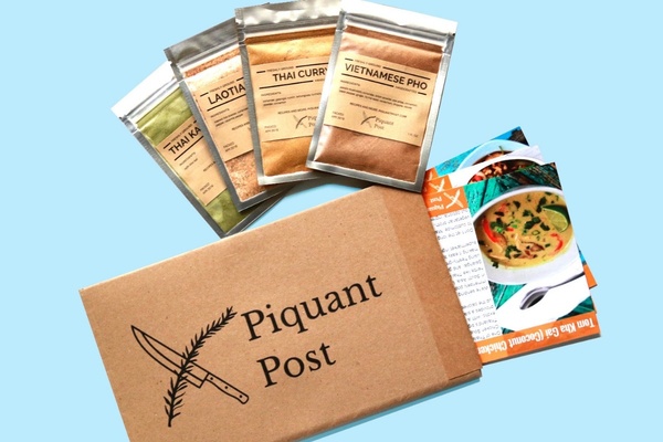 A Piquant Post subscription box with recipe cards coming out of it and 4 packets of seasonings.