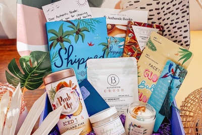An open Authentic Books subscription box including a book, book marks, candles, iced tea mix, and bath salts.