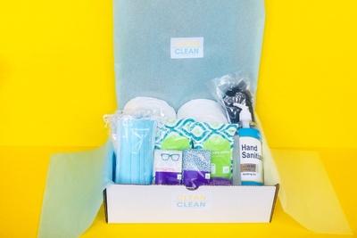 An open Clean Clean subscription box filled with hand sanitizer, glasses cleaner, face masks and other cleaning supplies.