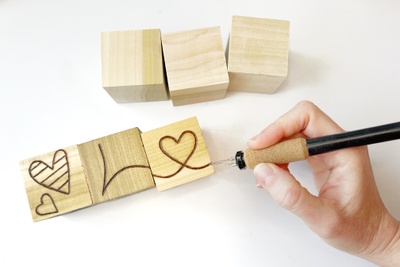 Seasonal blocks woodburning project on display. 3 blocks are being burned with hearts and letters that start to spell "Love". 