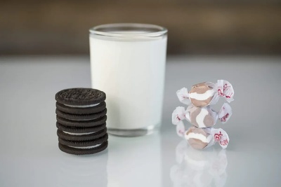 Stack of Oreos next to a cold glass of milk accompanied by a pile of cookies and cream saltwater taffy. 