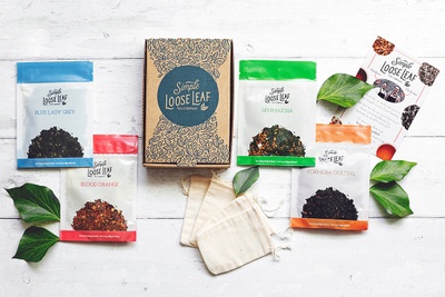 A closed Simple Loose Leaf Tea subscription box surrounded by colorful packages of tea and small, fabric bags.