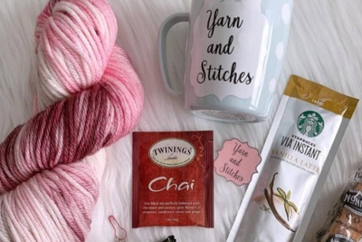 A Pink skein of yarn with varying shades as well as a custom mug, tea and instant coffee and biscotti