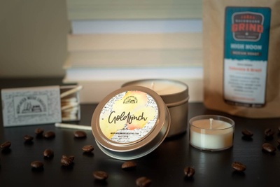 image of travel-sized candle in tin. The lid is off the candle and the label name of "Goldfinch" is visible. 
