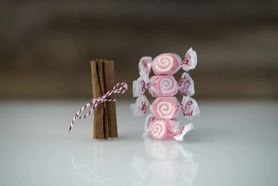 Cinnamon Saltwater Taffy stacked four high next to a bundle of cinnamon sticks wrapped in red and white twine. 