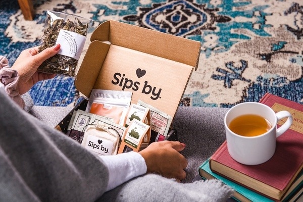 A woman opens a Sips by subscription box with various types of loose leaf tea and bagged tea.