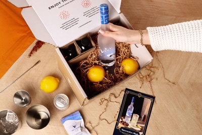 Image of someone unboxing a Cocktail Kit with a bottle of Grey Goose, fresh lemons, bar equipment, and a recipe card.