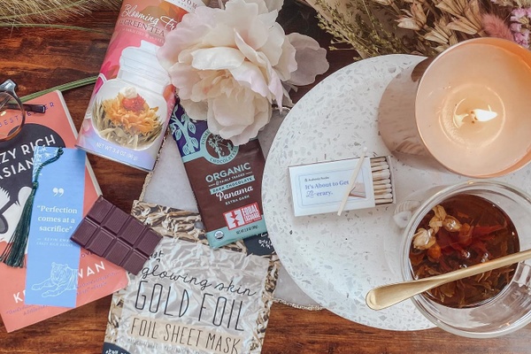 Items from an Authentic Books subscription box, including a lit candle, matches, tea, a chocolate bar and a flower.