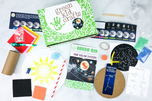 A Green Kid Crafts subscription box surrounded by astronomy cards, a crayon, colored paper and other craft items.