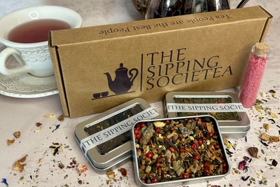 The Sipping Societea Loose leaf tea subscription box with tea tins and flavored sugar next to decorative tea cup.
