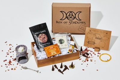 A closed Box of Shadows subscription box with a wax warmer, a packet of rose petals, some amber and a bracelet.