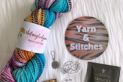 A multi colored skein of yarn including turquoise, orange and pink. A stitch marker and other items are also shown