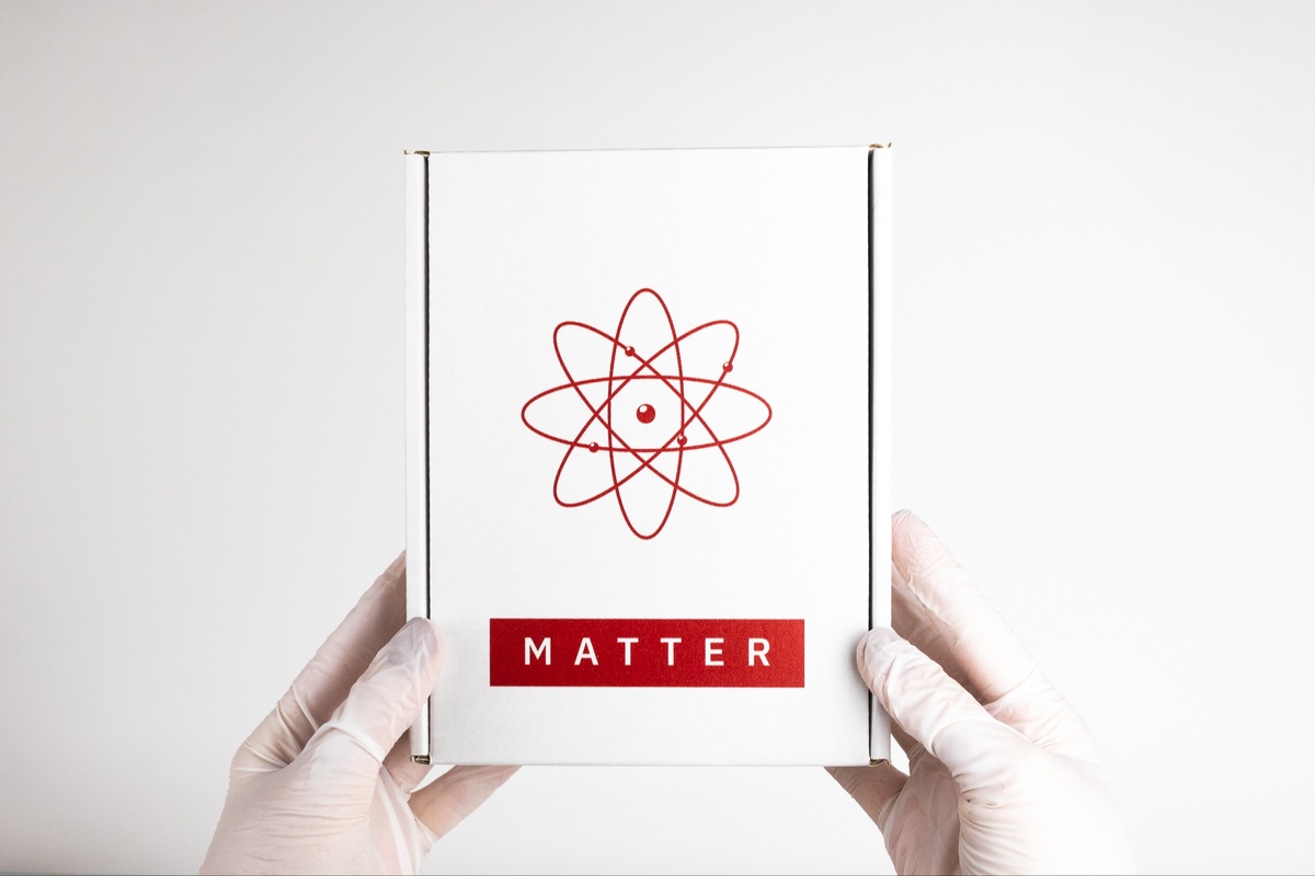 Gloved hands holding a closed, white Matter subscription box with an atom symbol on it.