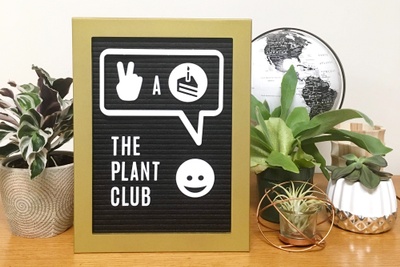 A sign that says The Plant Club, surrounded by various small potted plants.