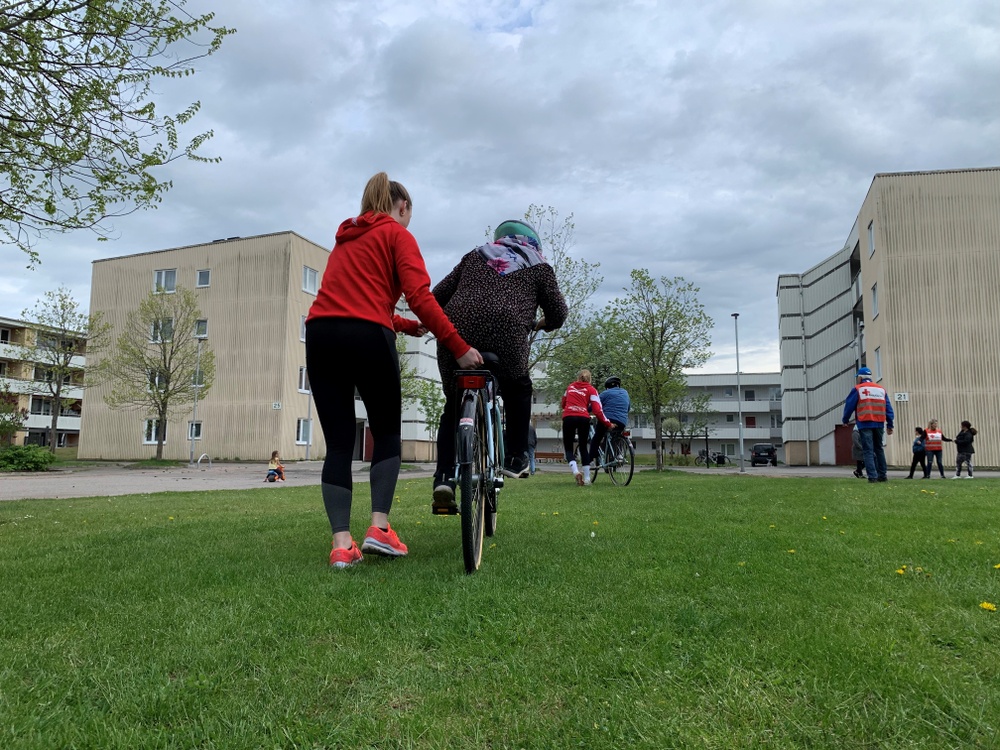 Kvinna i röda kläder hjälper en kvinna på cykel att hålla balansen 