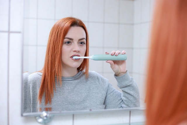 a 30yo women brushing her teeth with an electric toothbrush in front of the mirror
