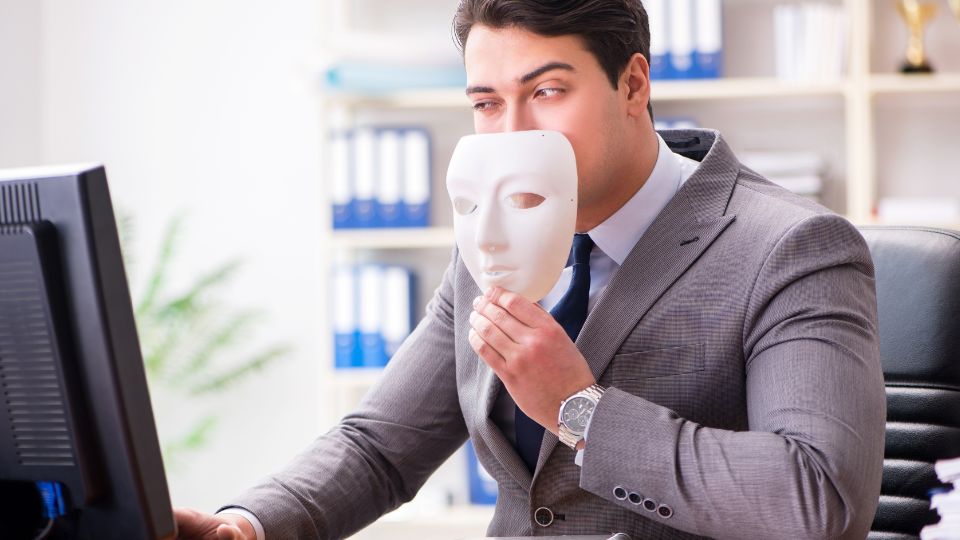 Man in grey suit wearing white mask looking at the computer