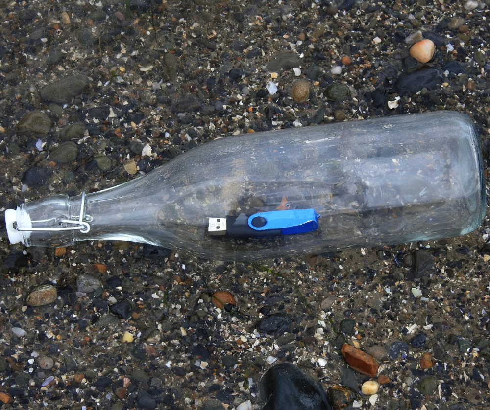 A USB  memory stick inside a clear glass bottle on a pebble beach.
