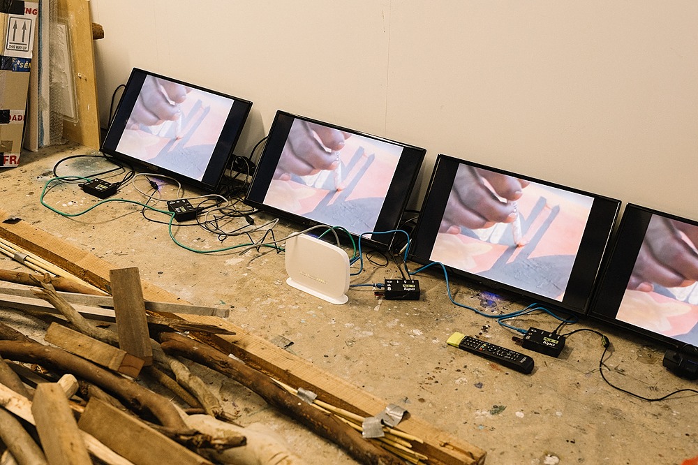 Brad Darkson's studio documentation. 4 screens lean against a wall, connected by cables. On the screens displays a close up detail of a hand painting.