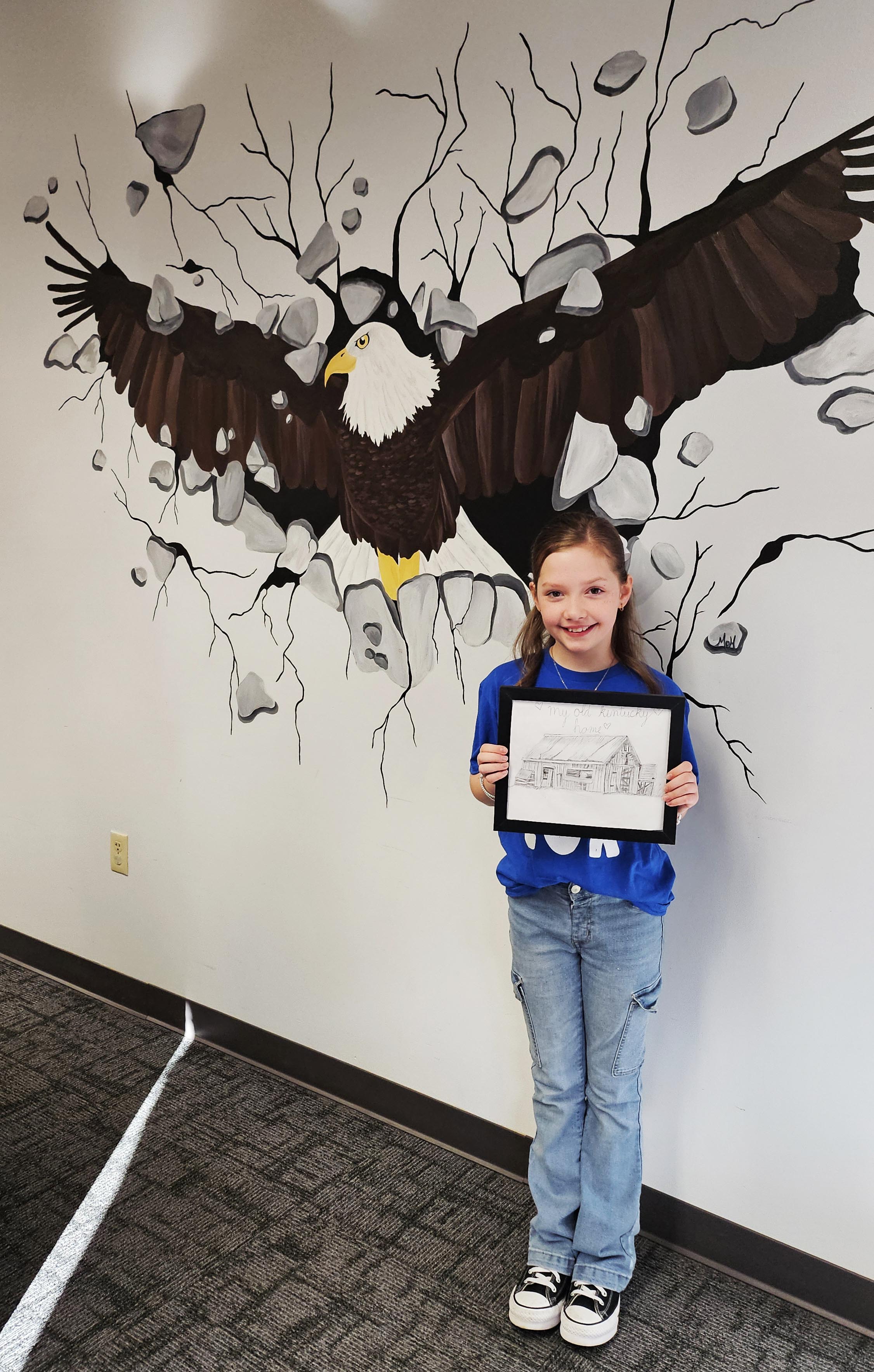 1 person stands in front of eagle drawing holding an artpiece.