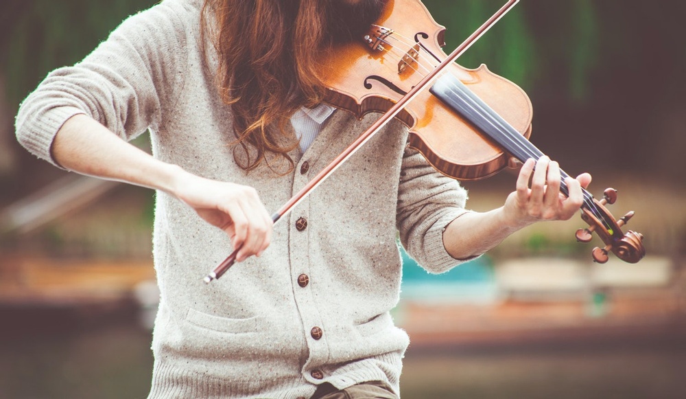En person med långt hår, men utan ansikte i bild, spelar på en fiol. 