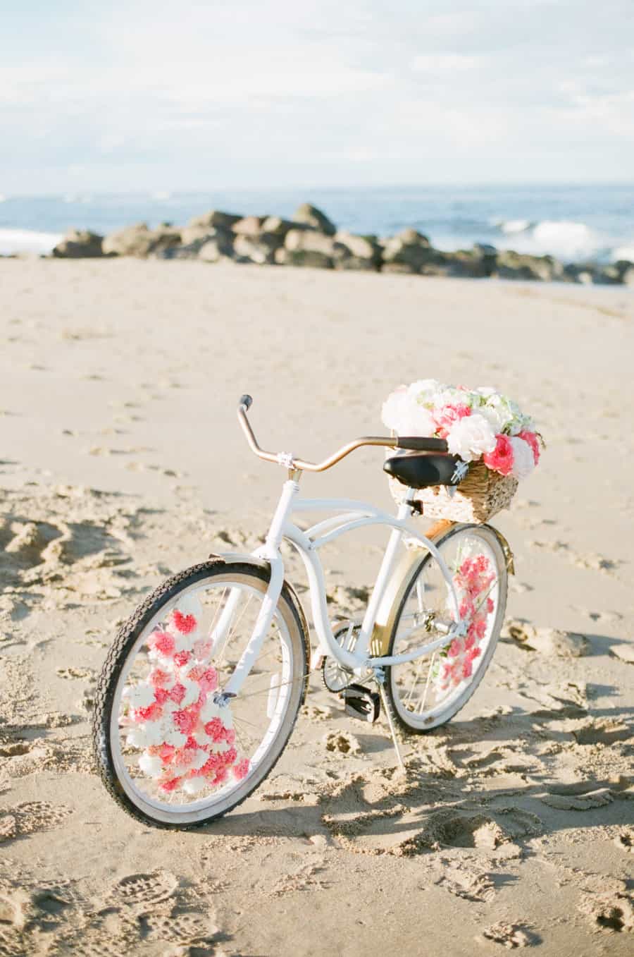 vélo blanc avec des fleurs dans le panier arrière sur une plage
