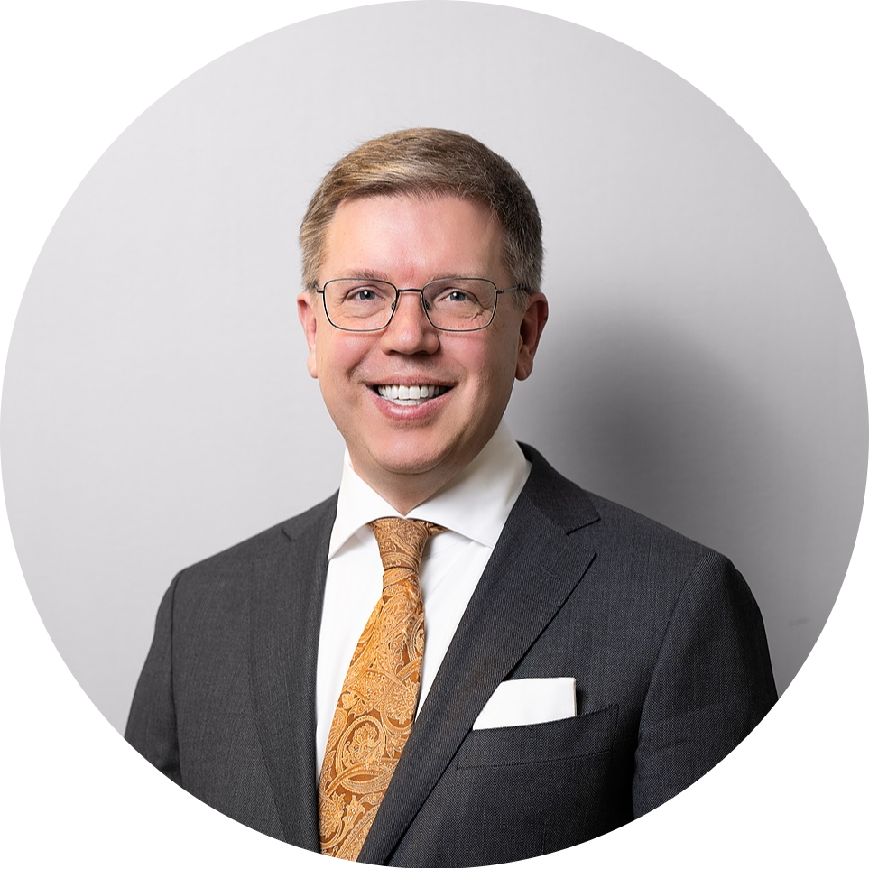 headshot of Joe Himali, a white man with blond hair wearing a grey suit with a yellow and orange decorative tie