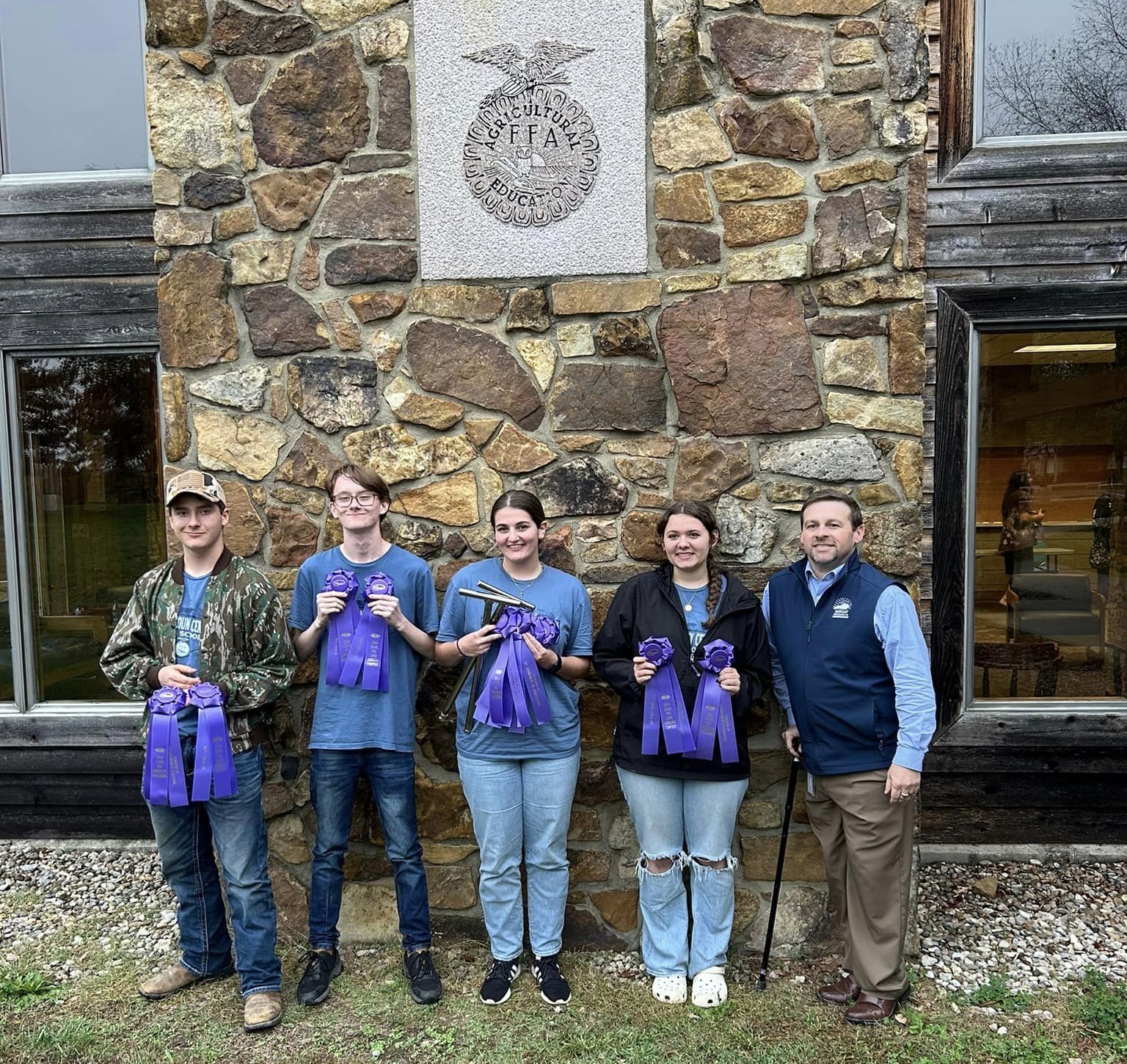 5 people stand in front of rock wall with FFA symbol on it. 4 of them are holding ribbons.