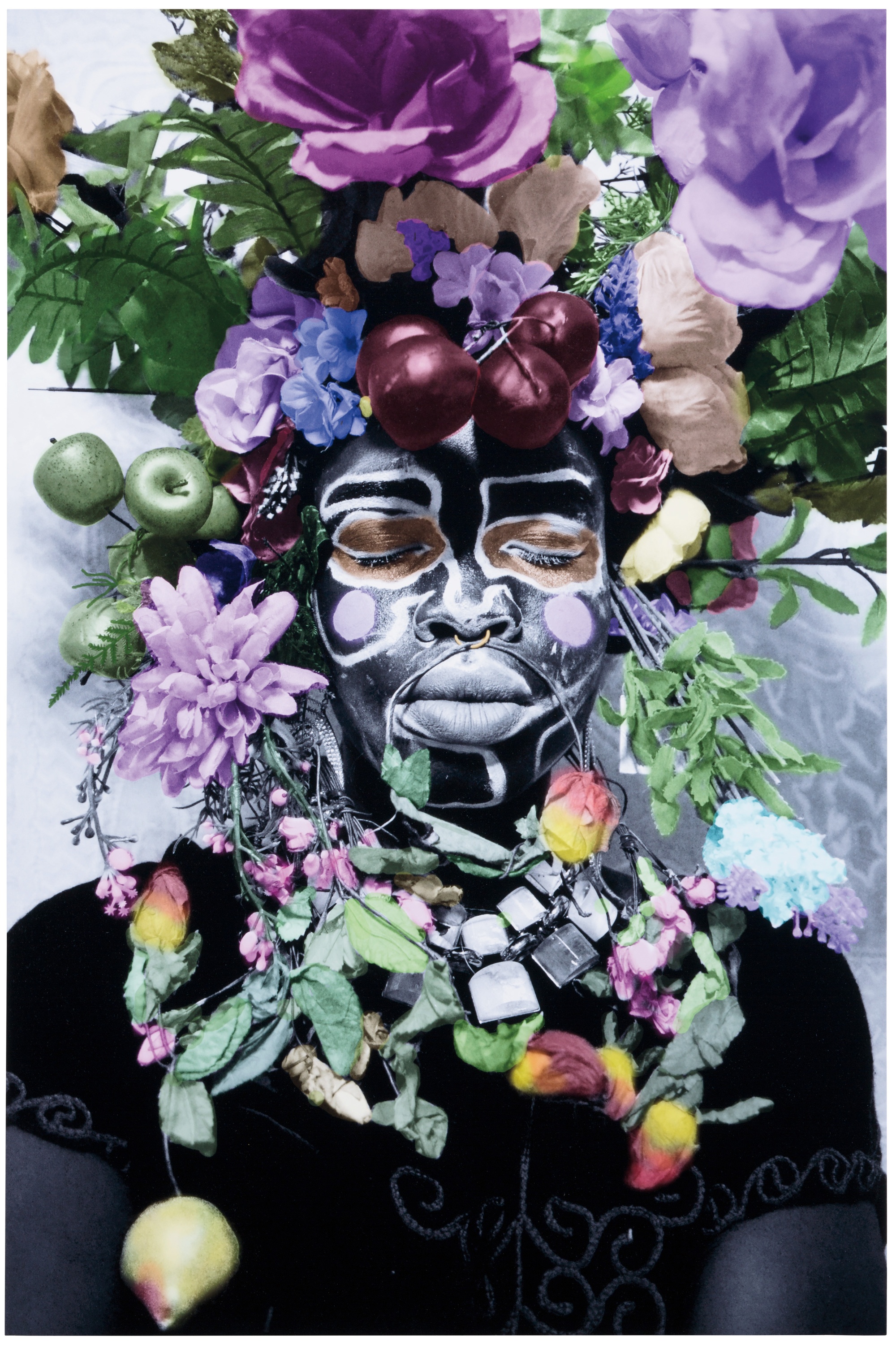 A photograph of a young, Black woman covered in black paint with green and purple flowers, leaves, and fruit draped around her neck and covering her head.