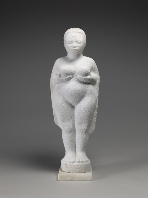 A white stone sculpture of a figure standing with hands cupping the underside of breasts and stippled texture.