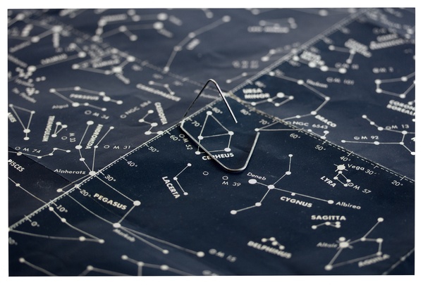 A photograph of a bent piece of thin metal sitting on a print of white circles and lines with the names of various constellations. 