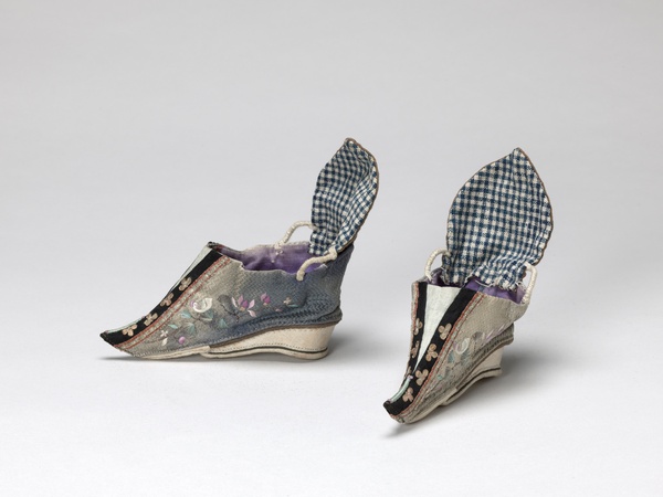 A gray pair of shoes with embroidered white birds, pastel purple lotus flowers, and pastel blue fanning leaves. Gold flower sequins on black fabric decorate the fronts.