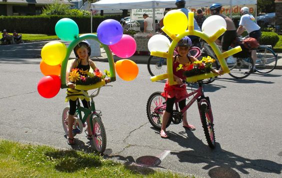 Kinder auf Fahrrädern mit Schwimmhilfen und daran befestigten Luftballons