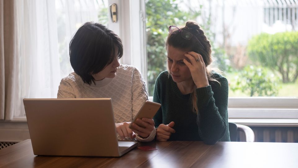 A woman in white upper is showing an older woman her phone