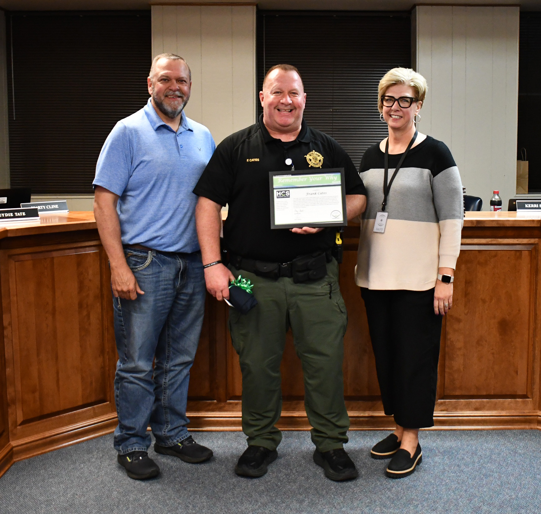 3 people smile for photo with 1 holding a framed certificate