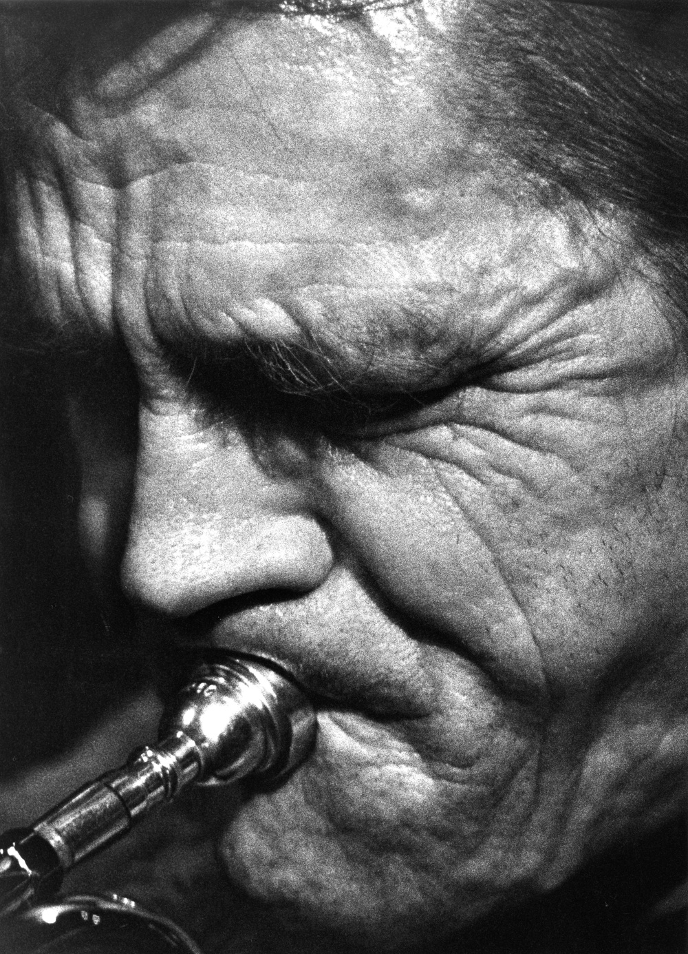 Svartvit närbild på Chet Bakers ansikte spelande på trumpet, ansiktet är vänt till höger i bild och ögonen är slutna.