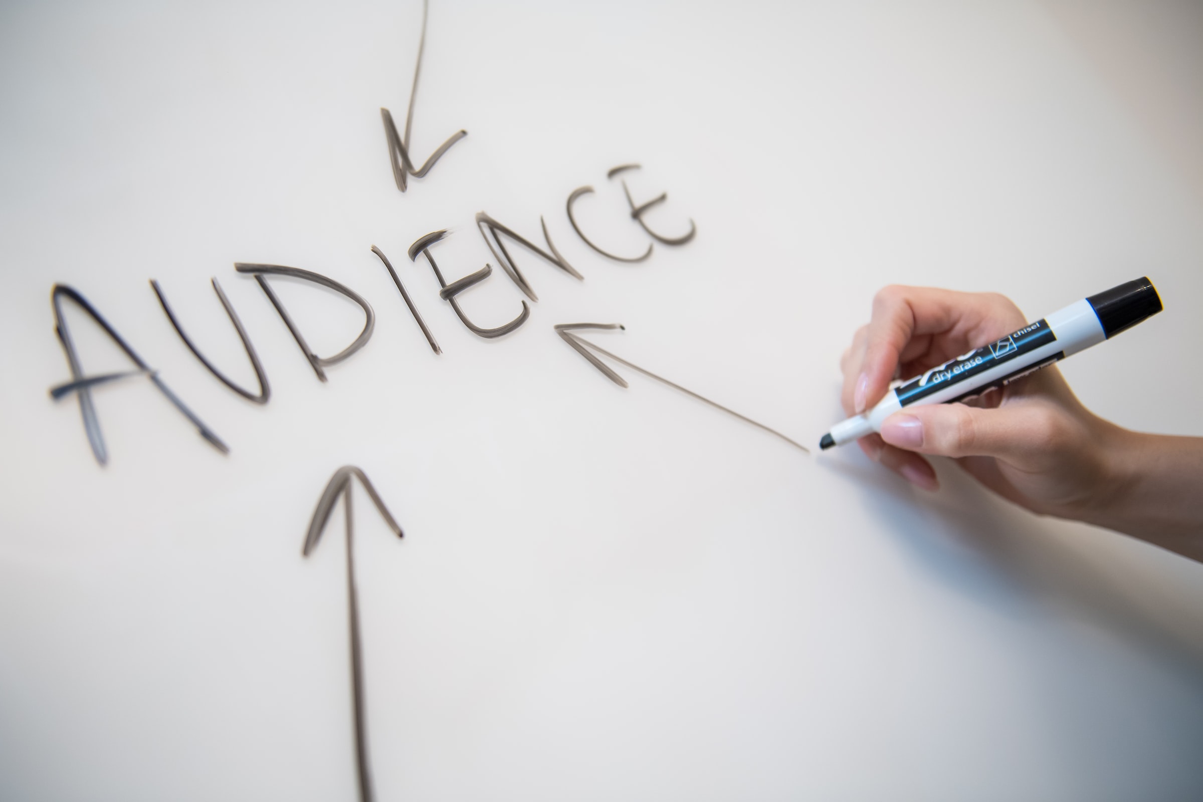 a hand holding a marker with 'audience' writing and three arrows on a white board stock image