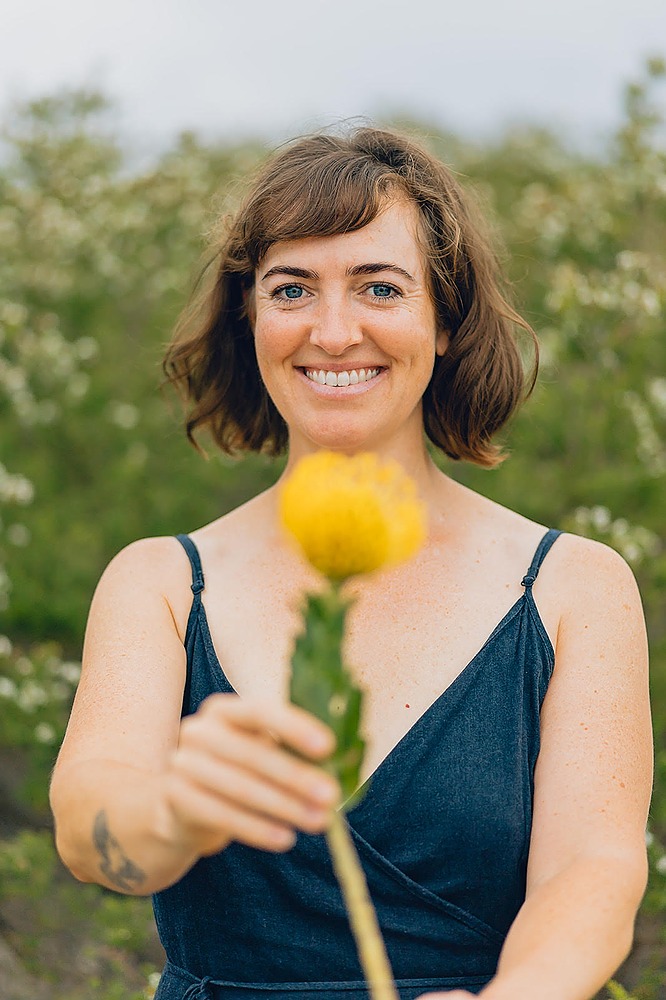 Woman standing in nature, holding a gorgeous yellow flower towards camera