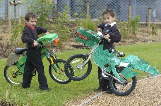 Zwei Kinder mit Fahrrädern, an denen Dinosaurier-Pappausschnitte befestigt sind