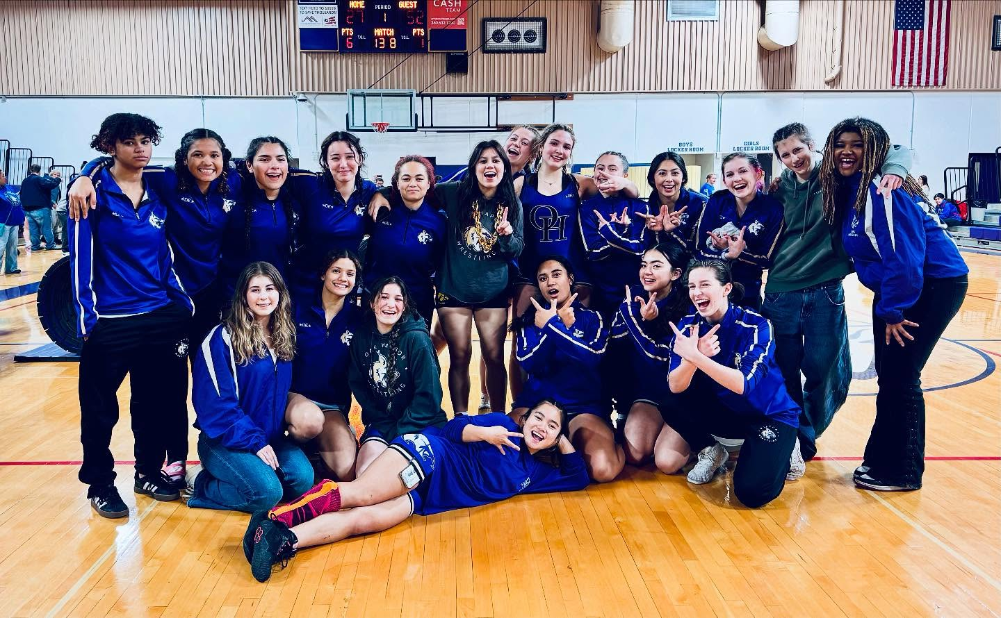 A group of young women in blue and gold uniforms pose for a photo on a basketball court.