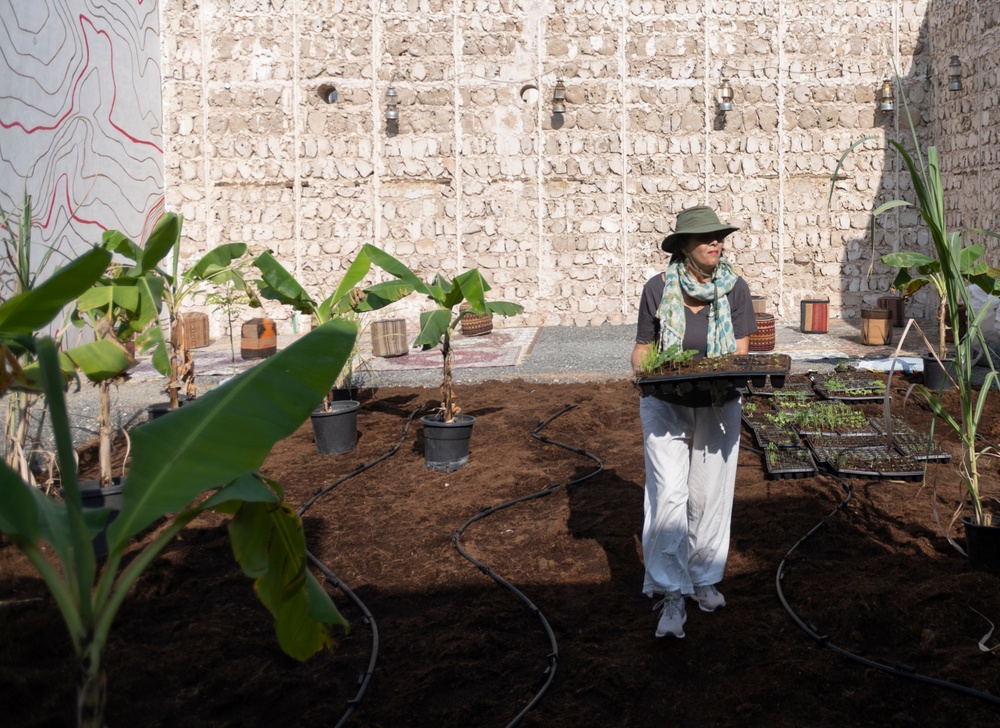 The Barbados based artist Annalee Davis carrying a tray of seedlings while working on the project Pray to Flowers – A Plot of Disalienation, 2022. for the Sharjah Biennale 2023.  Image courtesy of Sharjah Art Foundation. Photo Shavanas Jamaluddin