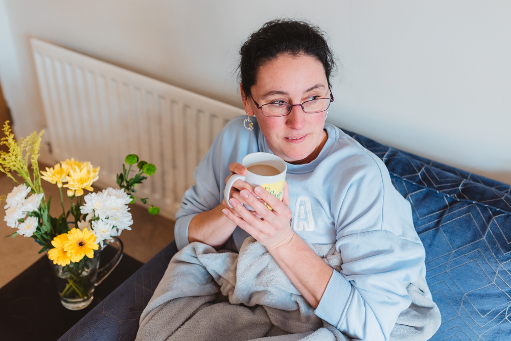 Helen holding a cup of coffee, sitting on a sofa next to a vase of flowers.