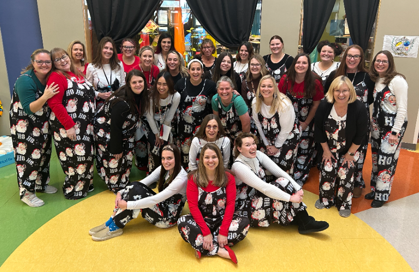 School staff are wearing matching Christmas jumpers and posed with smiles together.