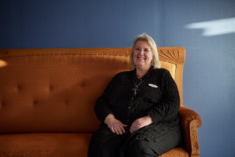 Bild på Suzanne Idsjö, anhörigsamordnare i Vara kommun, som sitter i en orange soffa som står framför en blå vägg.