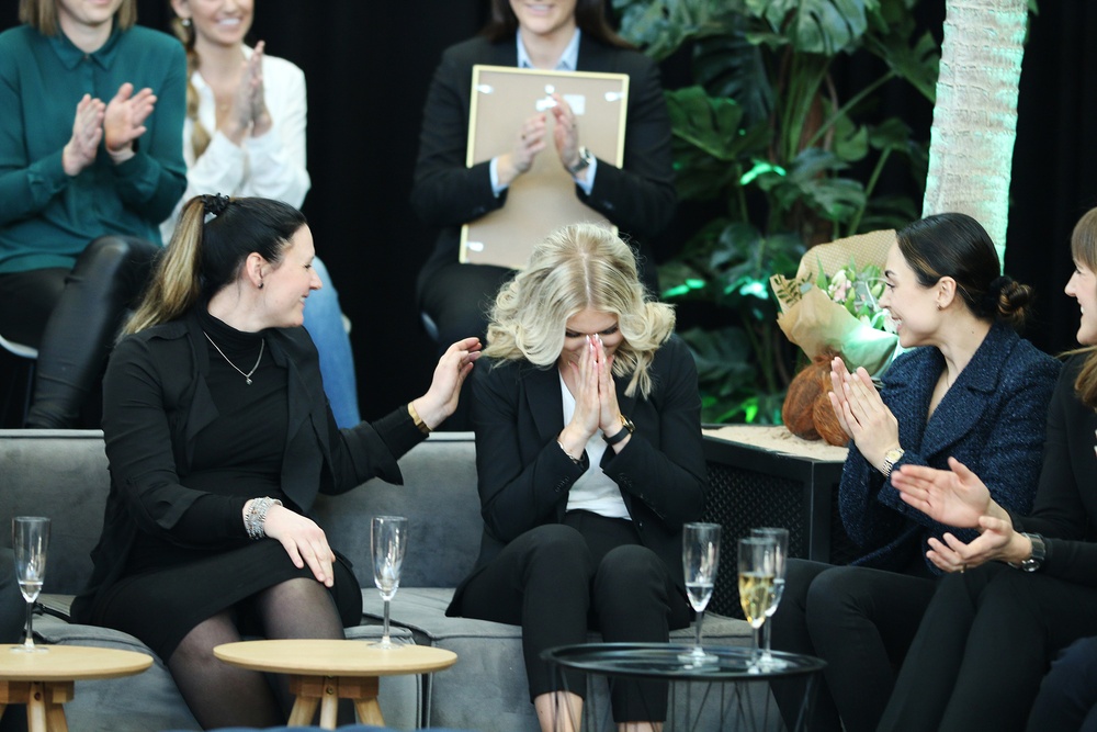 Årets unga ledande kvinna 2021, Therese Salmonsson, sitter i en soffa med Elin Angenfelt på vänster sida och Neda Babaabadi på högersida. Therese har precis utropats som vinnare och gömmer händerna i ansiktet medan de övriga nominerade applåderar.