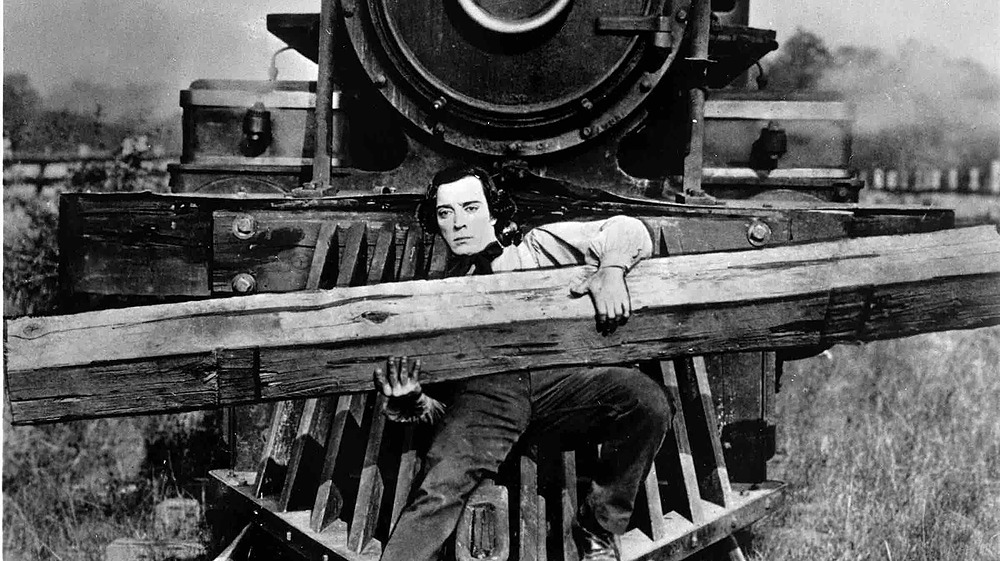 Man hangs on to railing in front of moving train in Buster Keaton The General silent movie