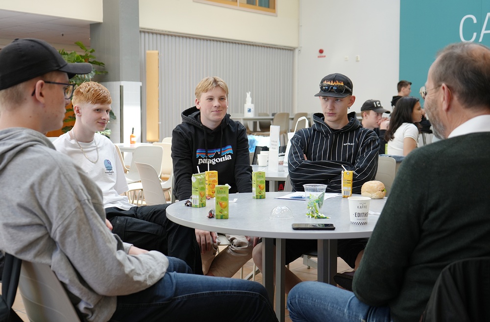 En grupp ungdomar sitter runt ett bord tillsammans med en lokal företagare och diskuterar affärsidéer.