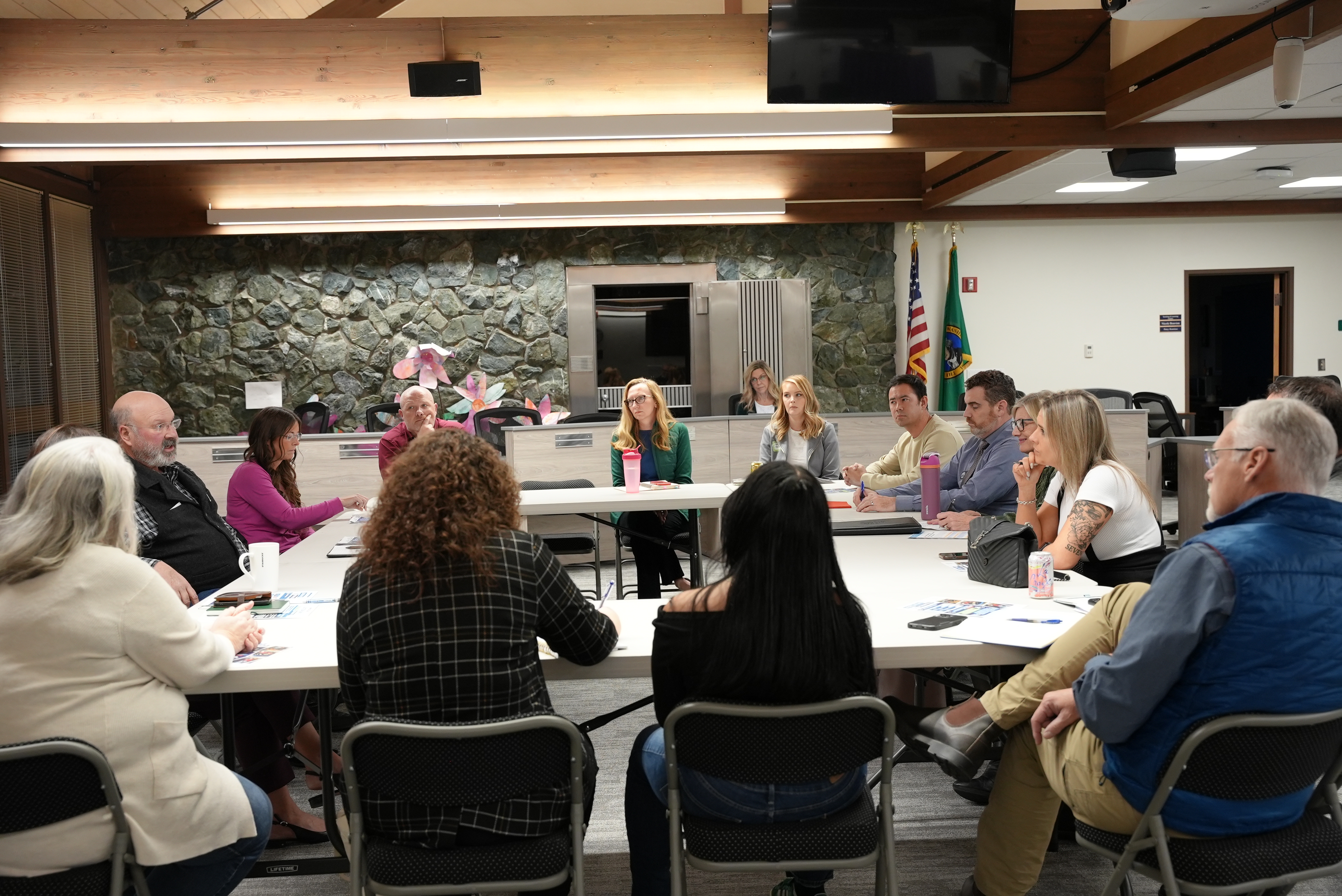 A group of people sit around a table in a meeting room, listening to a speaker.