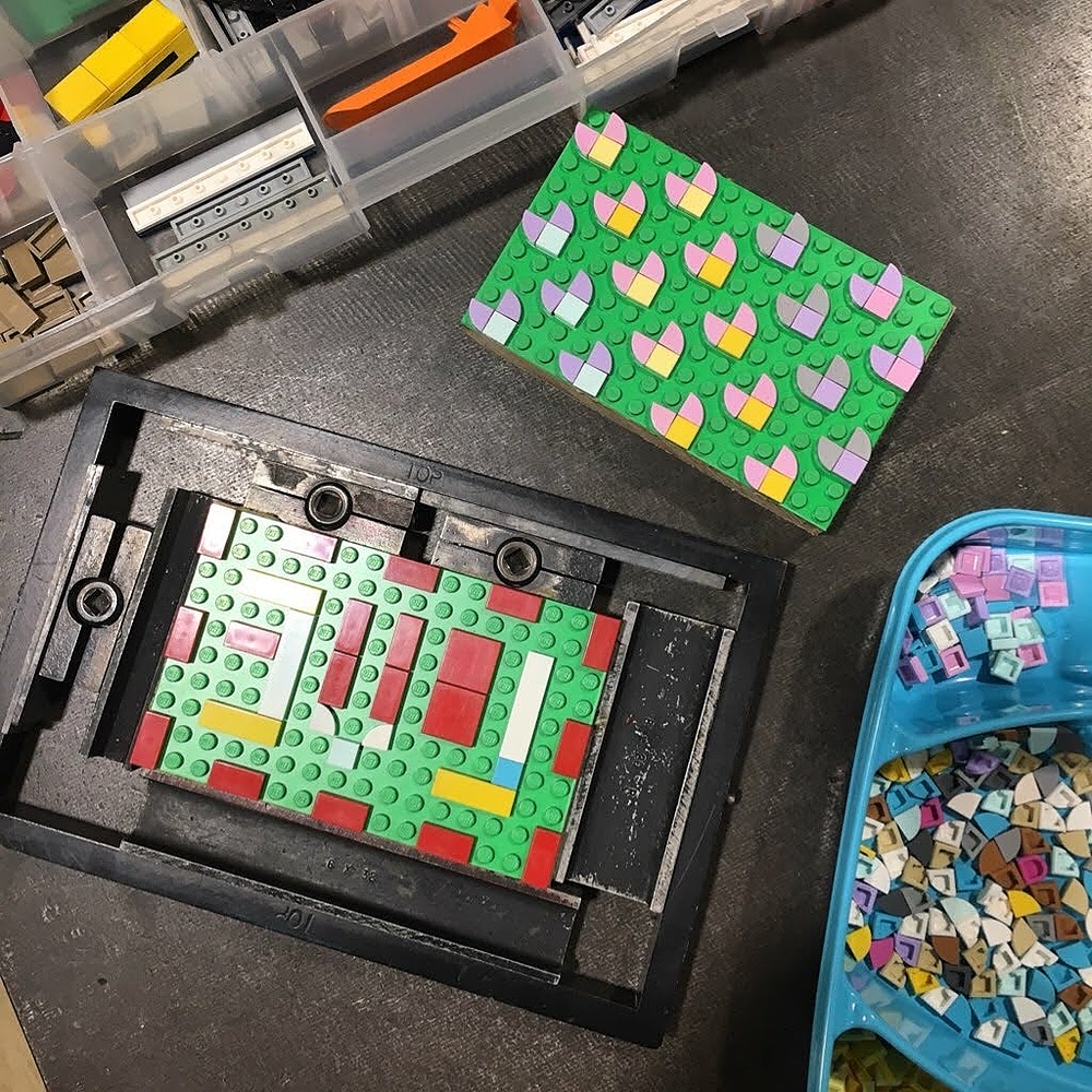 lego tiles on 2 different lego bases. One is locked into a printing chase and has an abstract design reading "love". The other has heart shaped patterns all across the lego base.